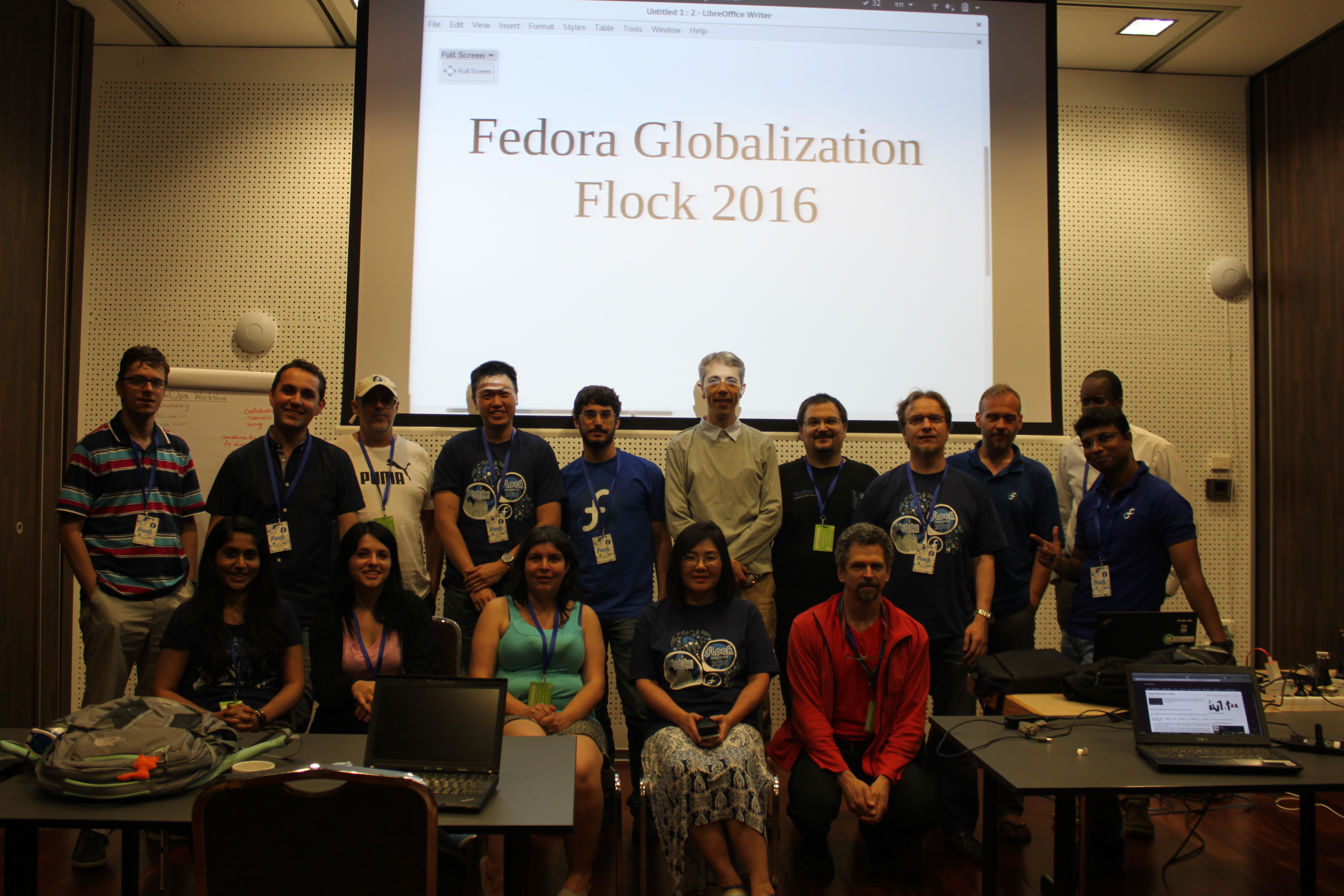 Um grupo de cerca de 15 pessoas em pé para uma foto na frente de uma tela de projetor com um slide que diz 'fedora globalization flock 2016`